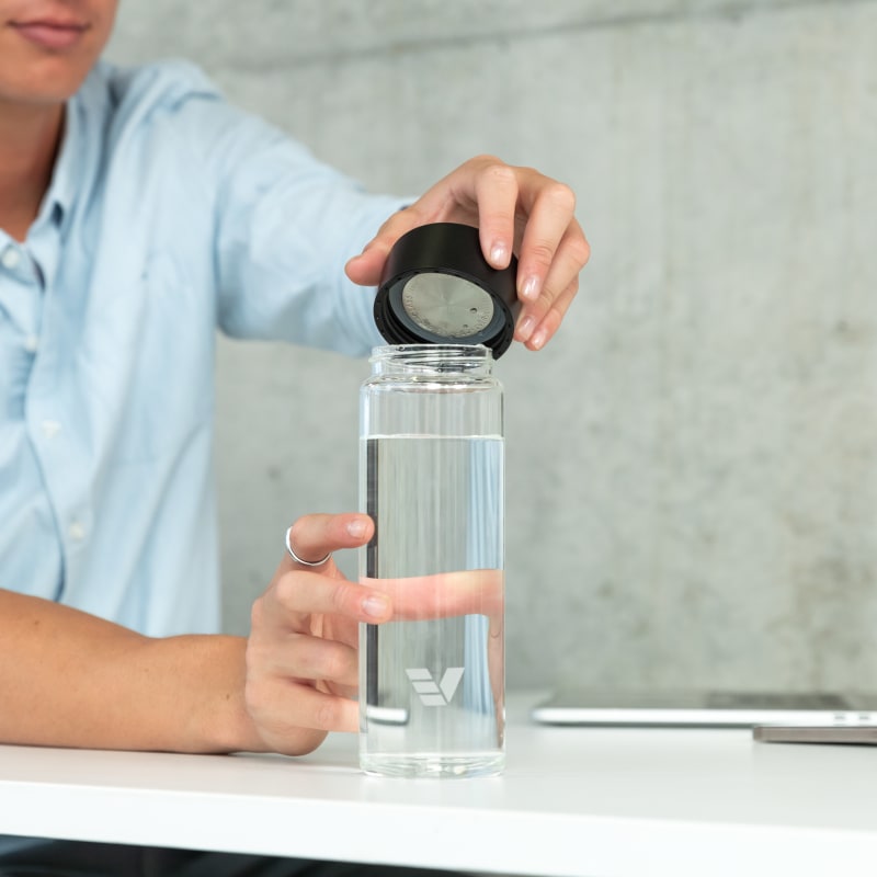 A male taking off the black lid from his Ever Vessel Glass water bottle at his desk.