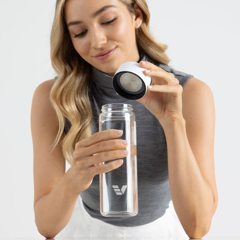 Female holding her optically clear borosilicate glass water bottle, with white lid off at the office.