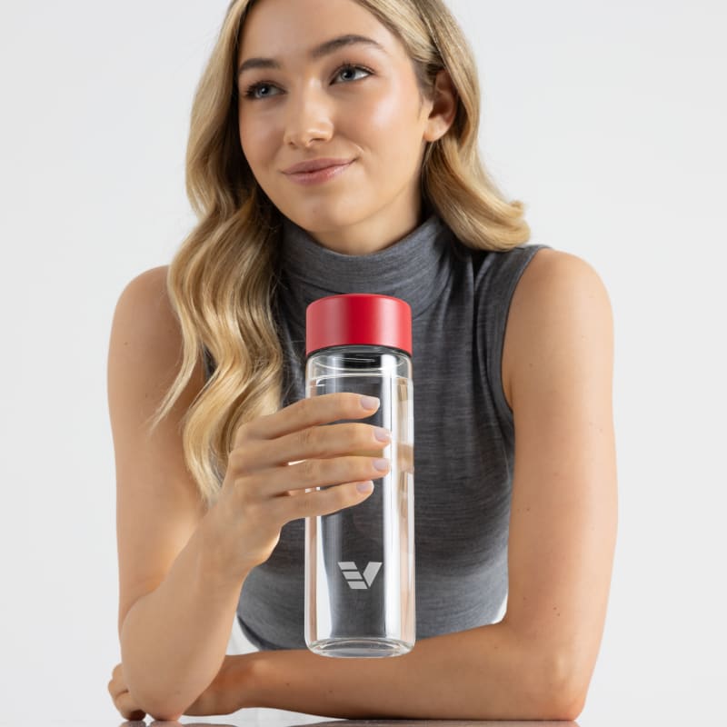 A female holding her Ever Vessel Glass water bottle with red lid above a stone bench at work.