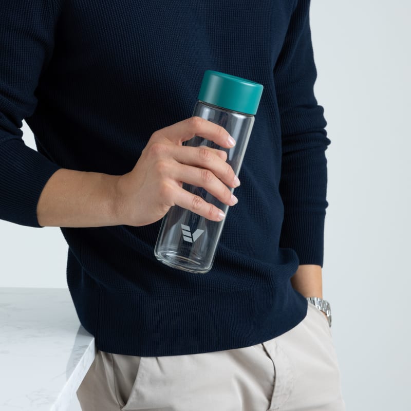 A male holding his Ever Vessel Glass water bottle with teal green lid next to a stone table.
