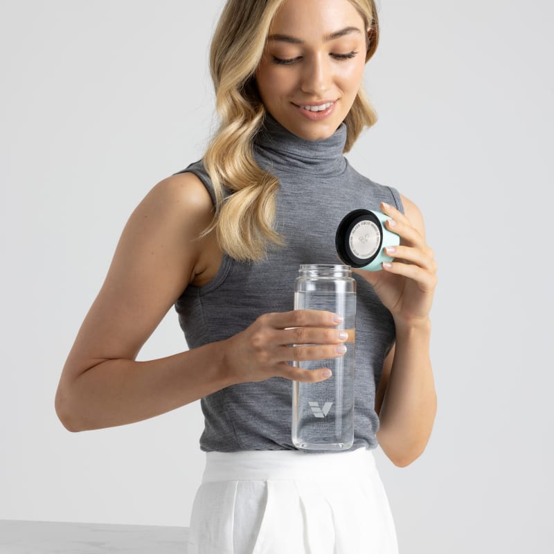 A female removing the lid from her Ever Vessel Glass water bottle with mint green lid at the office.