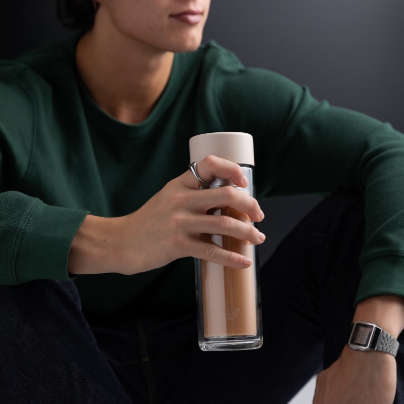 A male holding an Ever Vessel Glass Multi double walled tea flask bottle with Desert beige colored lid and milk tea inside.