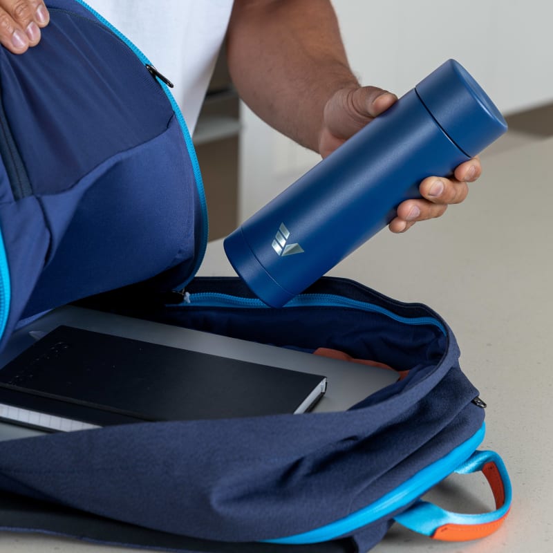 A male packing his Ever Vessel Multi Blue stainless steel tea infuser water bottle into his backpack.