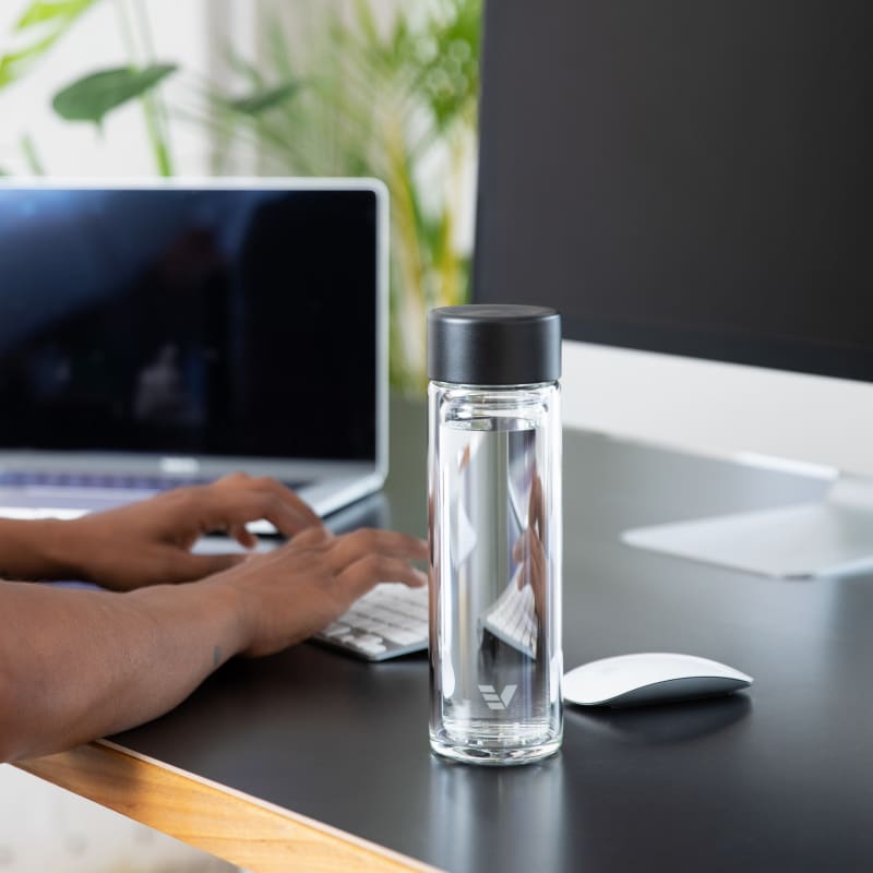 A male at his desk next to his  Ever Vessel Glass Multi glass double wall tea infuser water bottle with black lid.