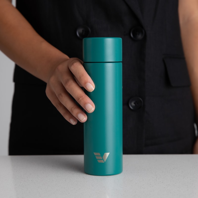 Female holding her Ever Vessel Mini Teal green small water bottle at a stone bench.