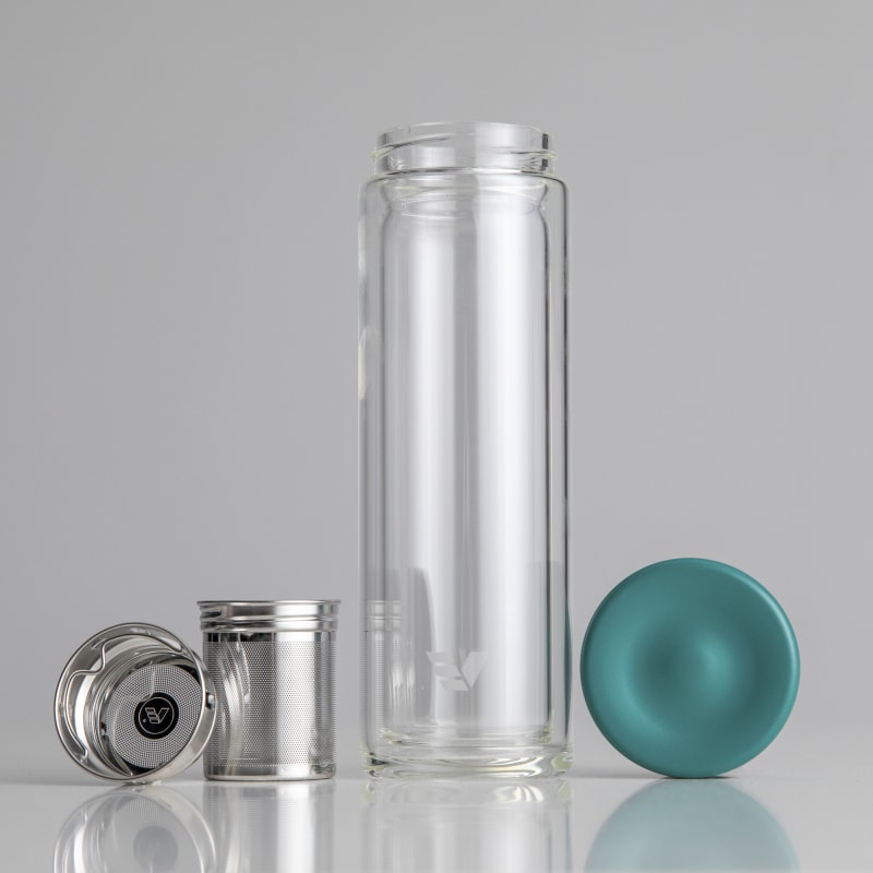 A Glass Multi tea infuser flask bottle sitting on a bench with the tea infuser and lid sitting separately.